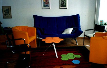 Beratungsraum mit blauem Sofa, orangefarbenen Sesseln und Bildern an der Wand